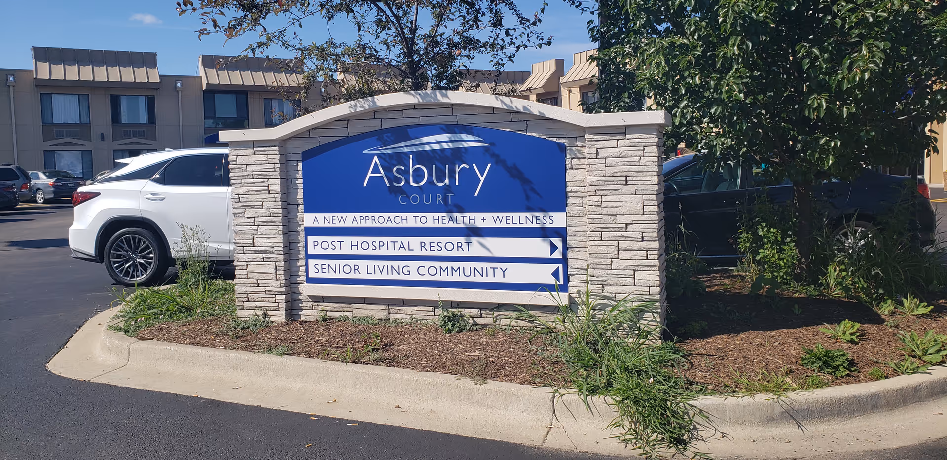 Asbury Court sign in front of a senior living campus with parked cars.