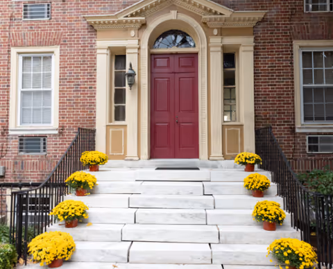 Front entrance steps with a maroon door and yellow potted flowers on both sides.