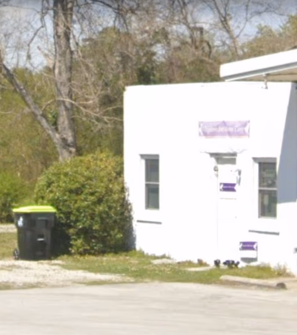 White building exterior with purple sign and green trash bin outside