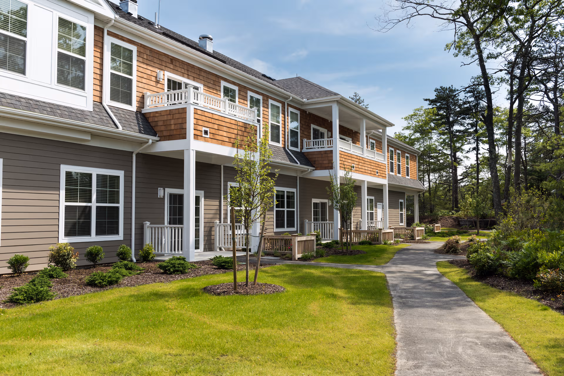 Exterior view of a multi-unit senior living building with balconies and a walking path.