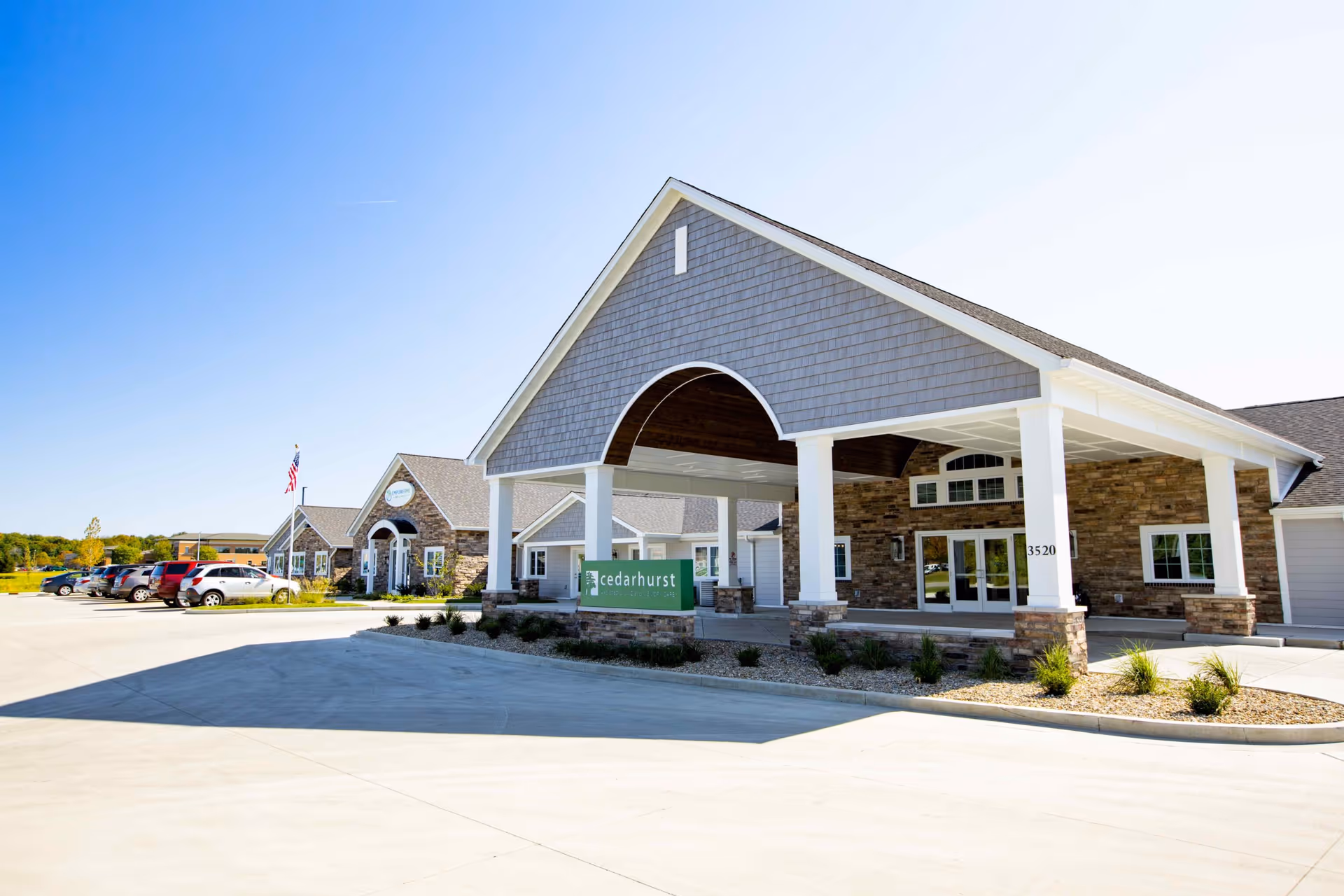 Front entrance and porte-cochère of Cedarhurst Senior Living with parked cars and a clear blue sky.
