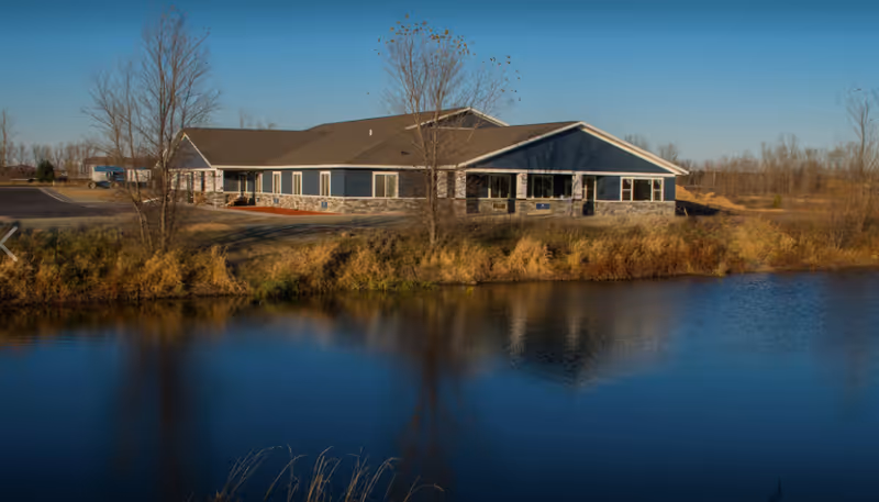 BeeHive Homes facility sits beside a calm lake with trees nearby.