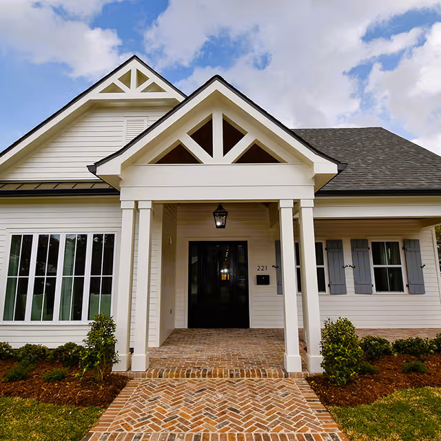 Front entrance of a white senior living facility with a brick pathway and landscaping.