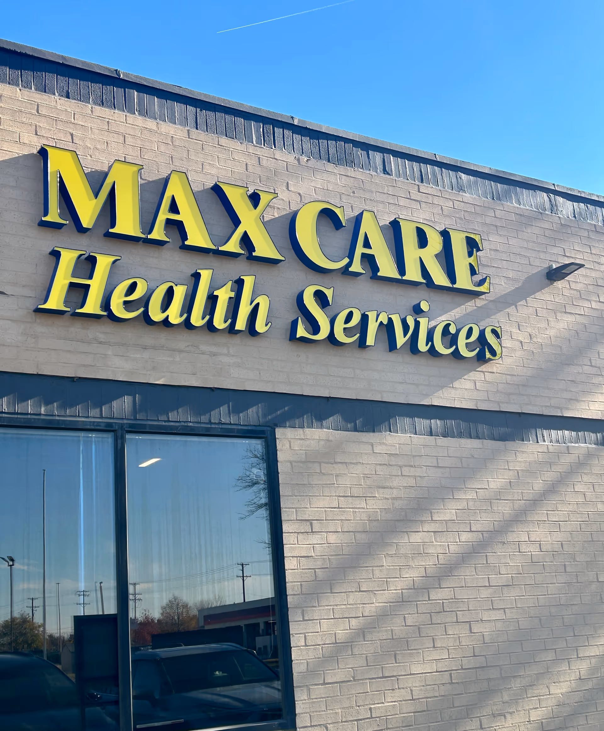 Exterior view of a brick building with a yellow Max Care Health Services sign.