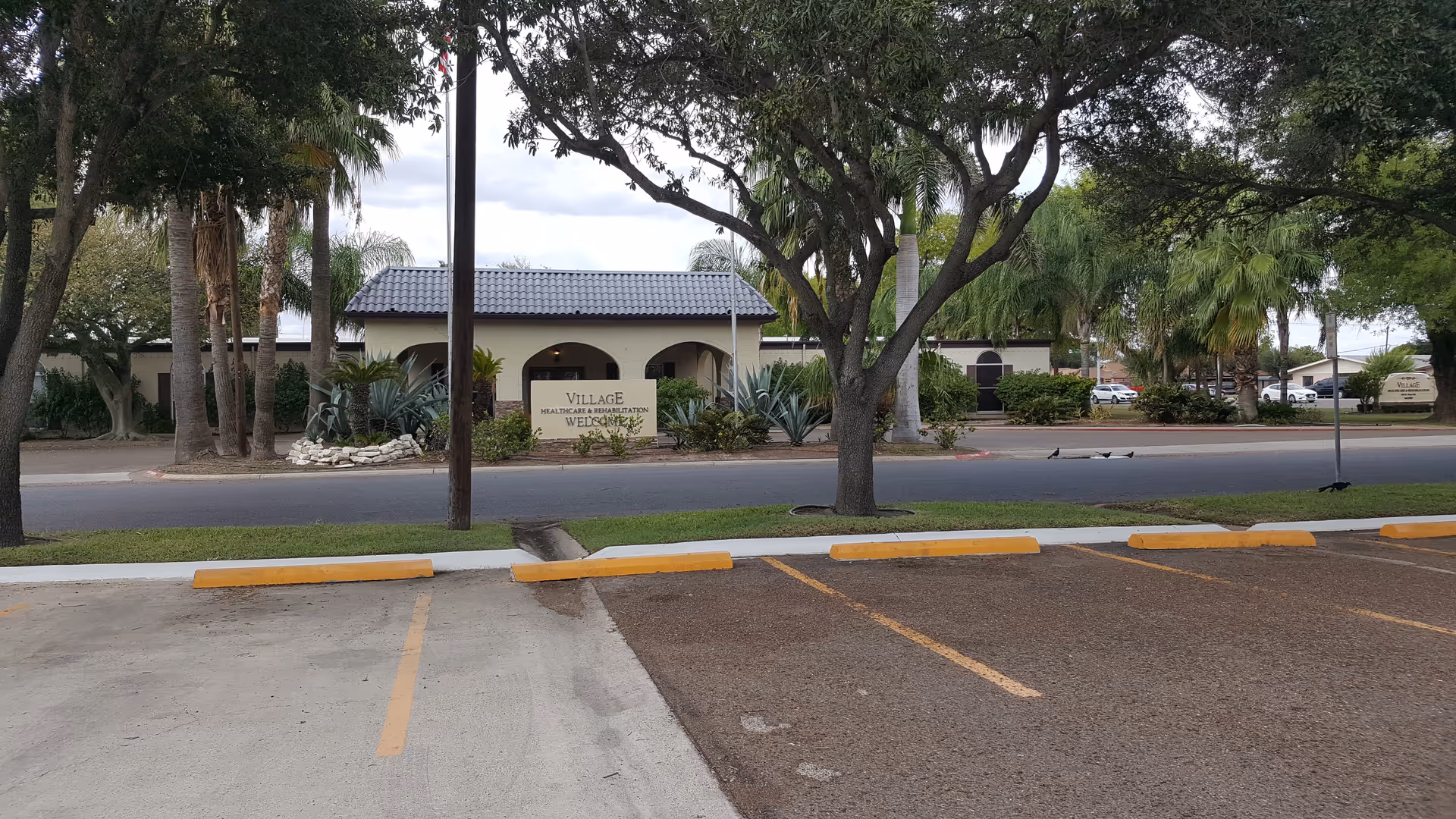 Exterior view of Village Healthcare and Rehabilitation entrance with trees and parking.