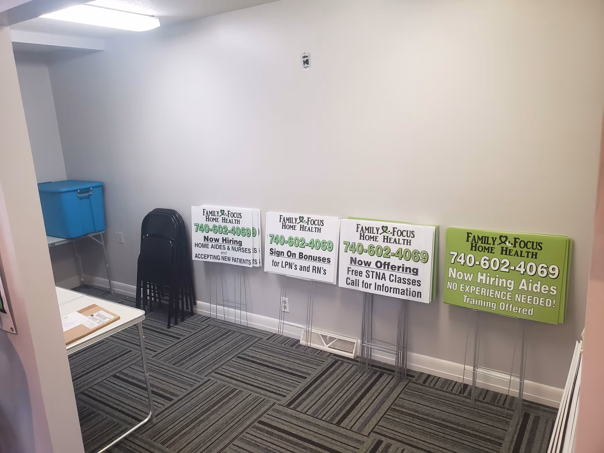 Empty room with stacked chairs and signs advertising Family Focus Home Health jobs.