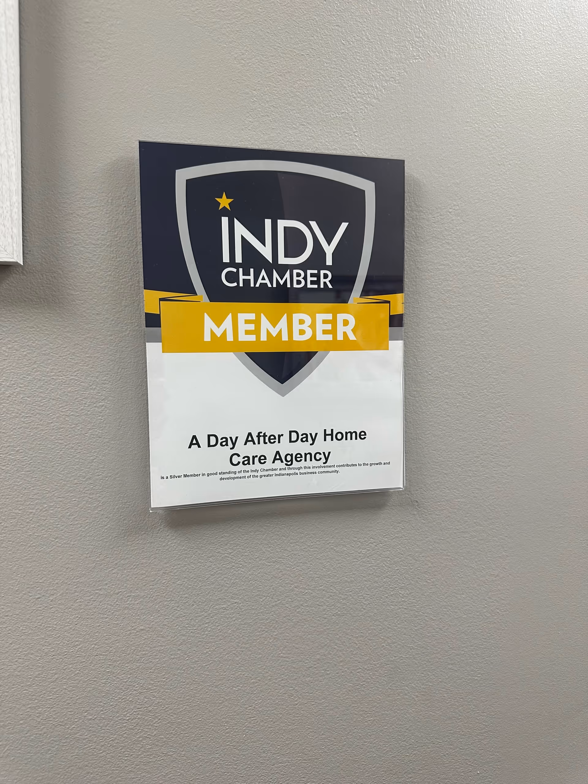 Wall-mounted sign on wall reading Indy Chamber Member and A Day After Day Home Care Agency.