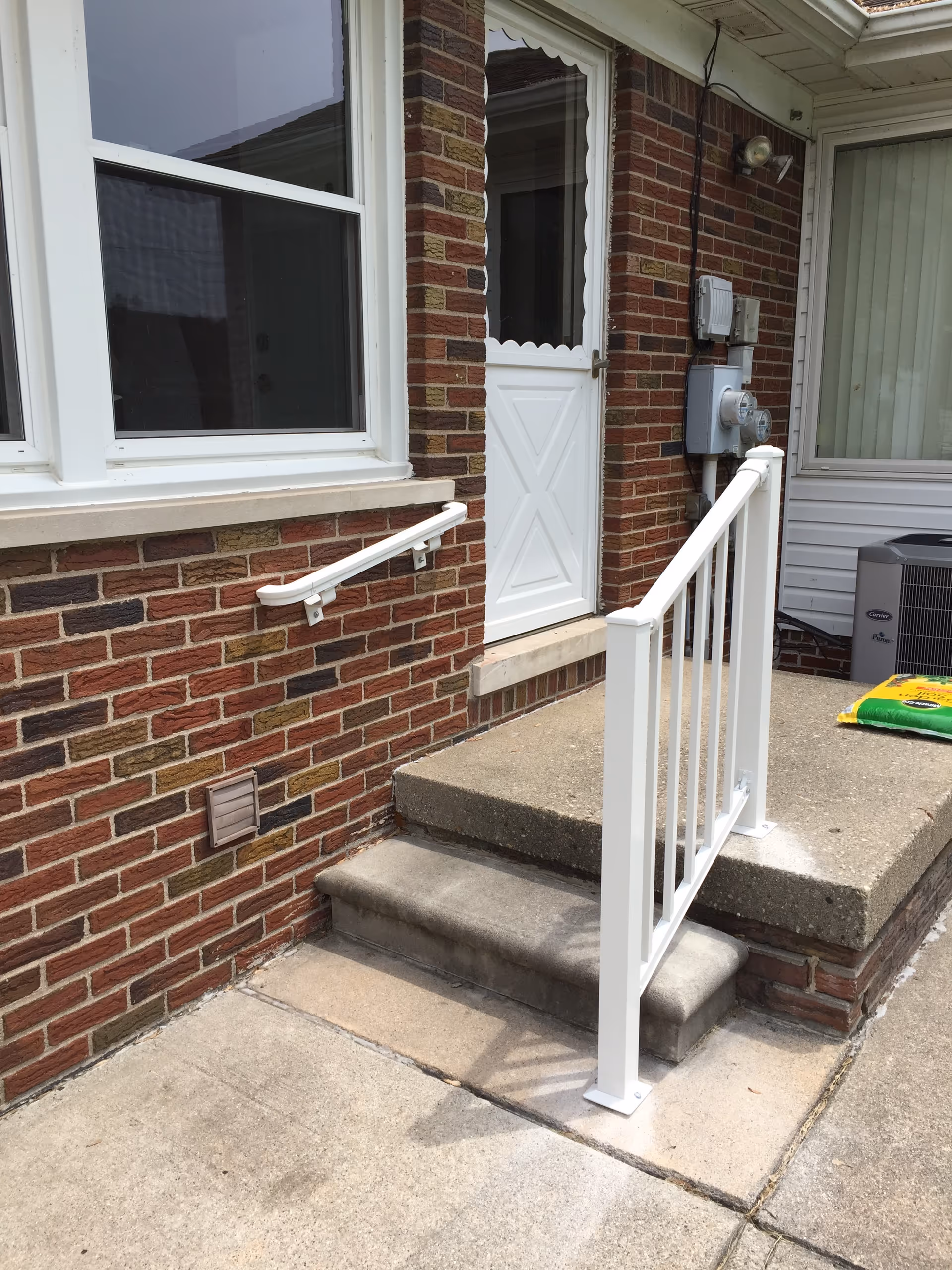 Brick exterior entrance to a senior living home with white door, steps, and railing