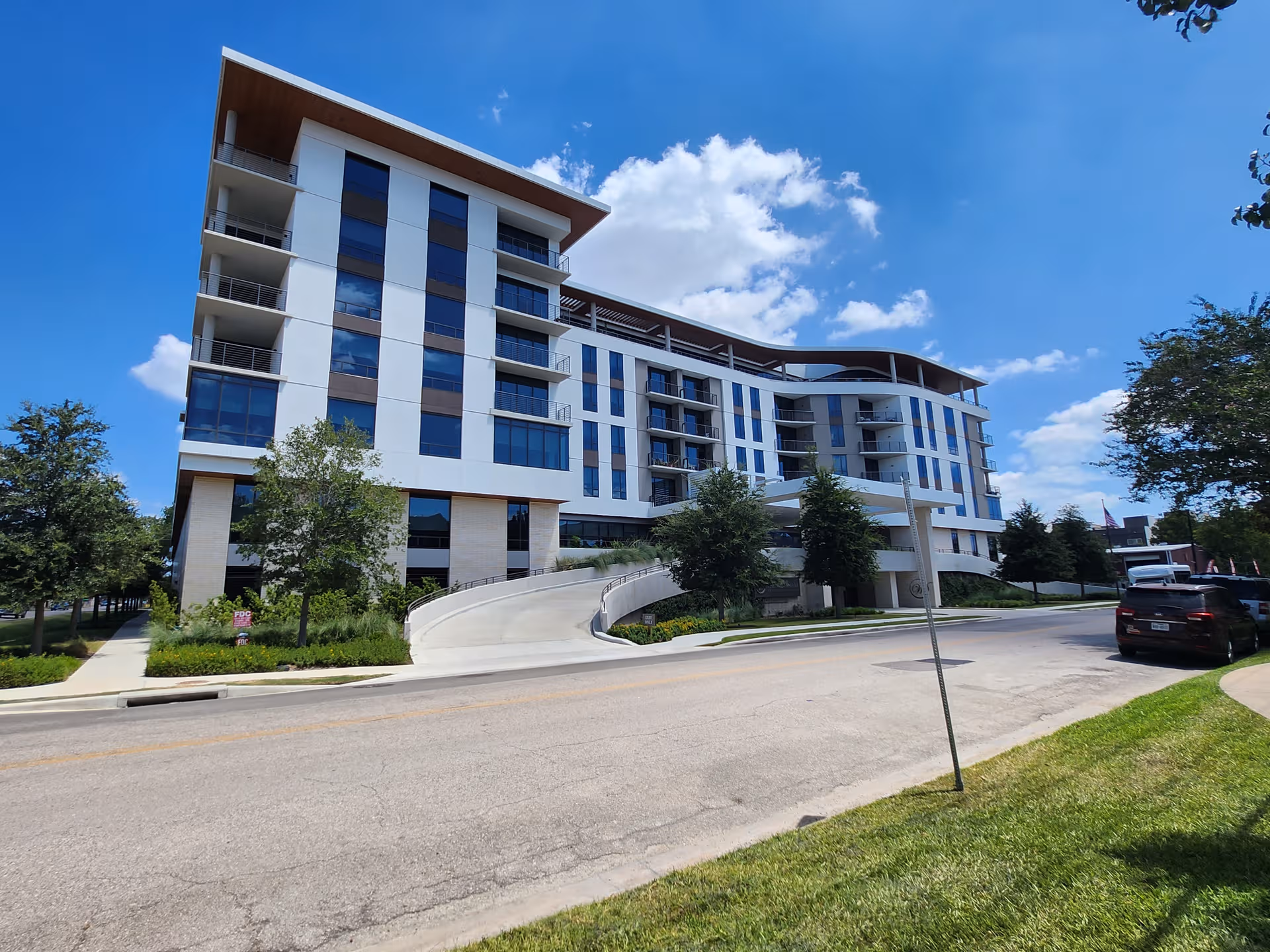 Modern multi-story senior living building with a curved ramp and landscaped surroundings.