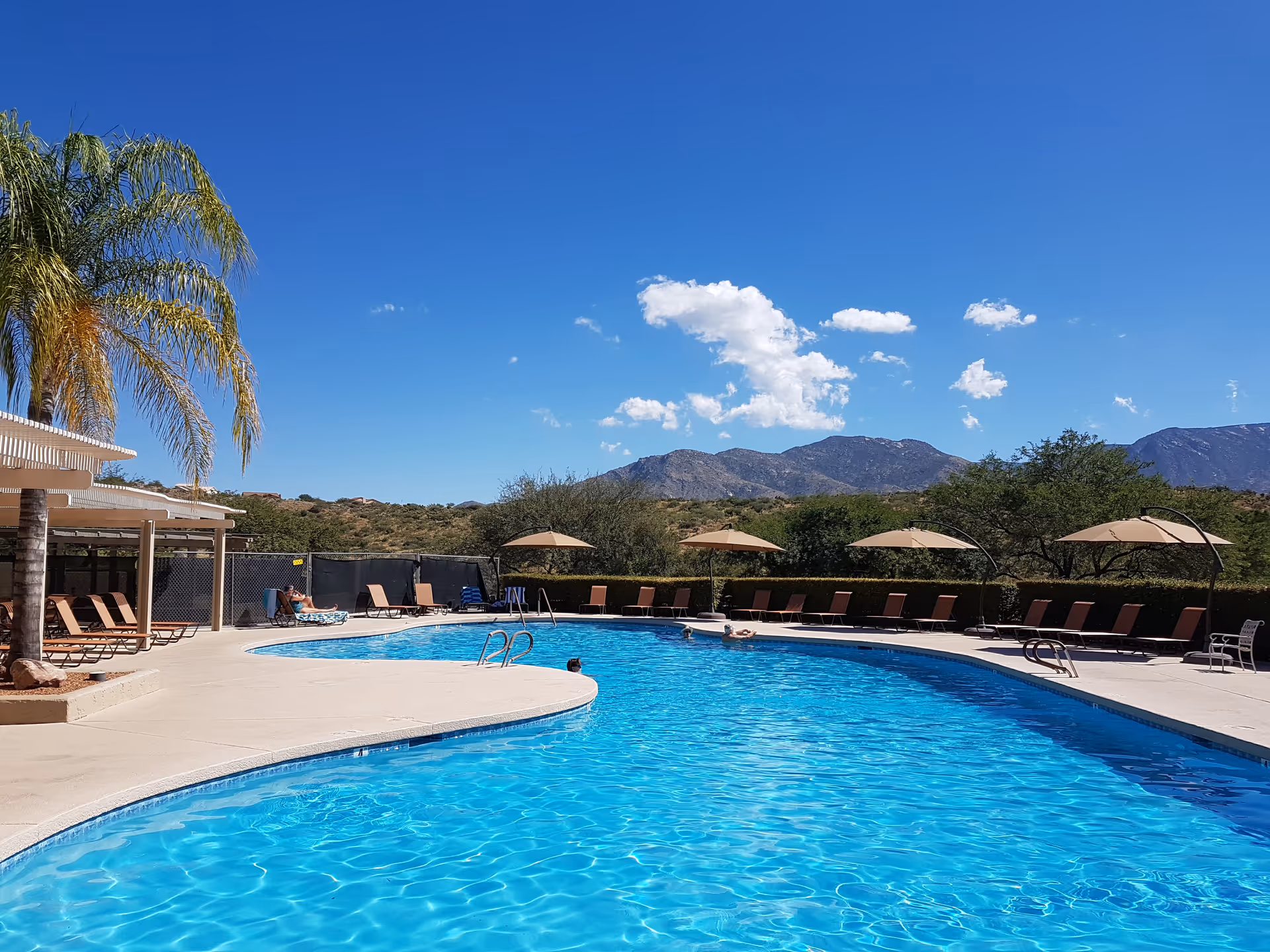 Sunny outdoor pool area with lounge chairs and umbrellas against desert mountains.