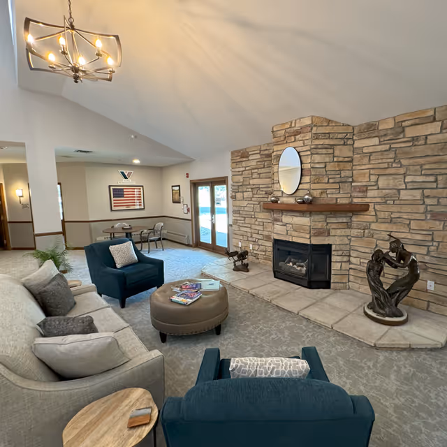 Cozy living room with stone fireplace, seating, and decorative sculptures in a senior facility.