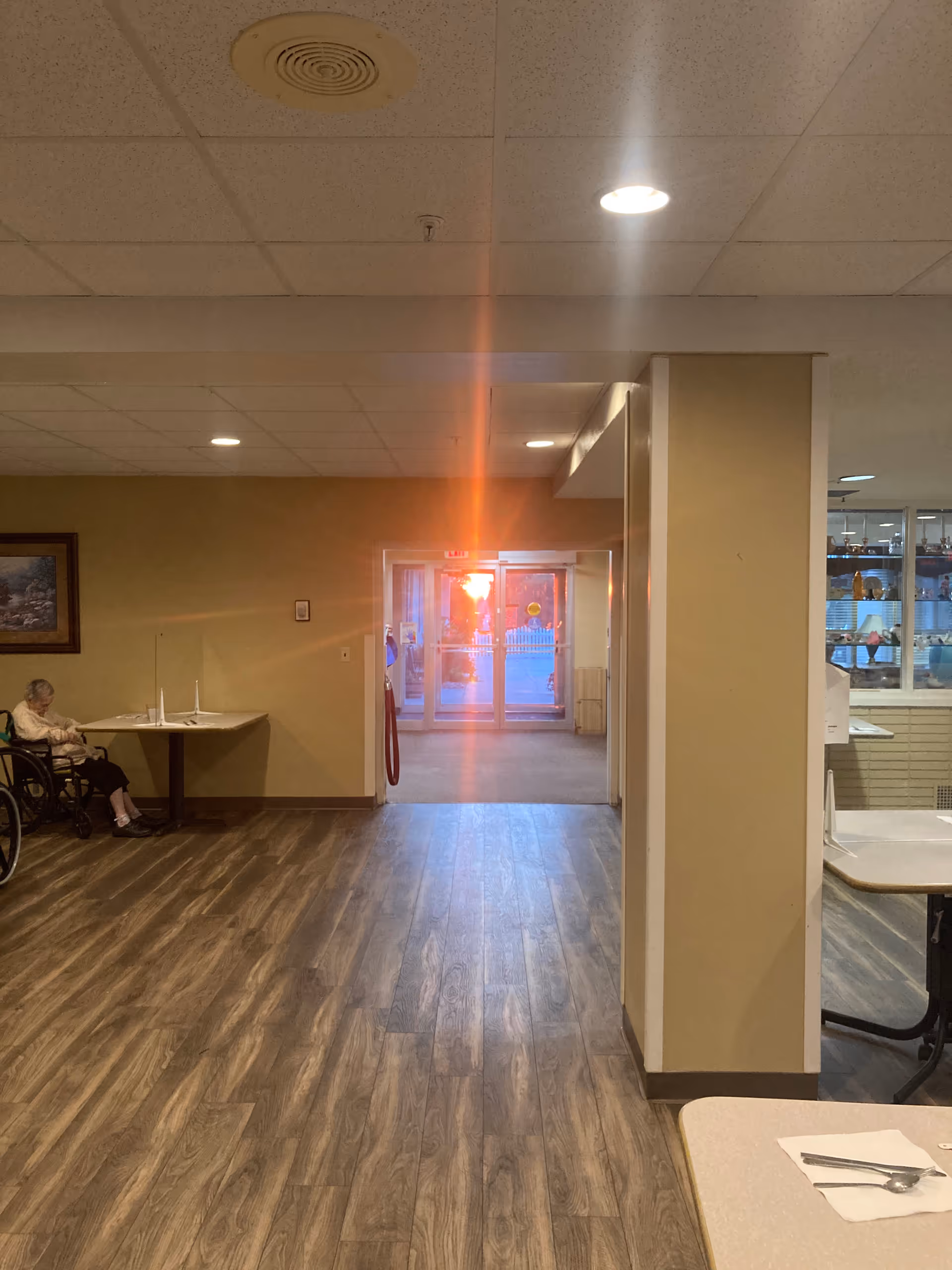 Long hallway in a senior living facility with a seated resident on the left.
