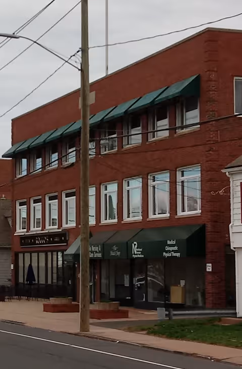 Brick, three-story building with green awnings and storefronts along a sidewalk.