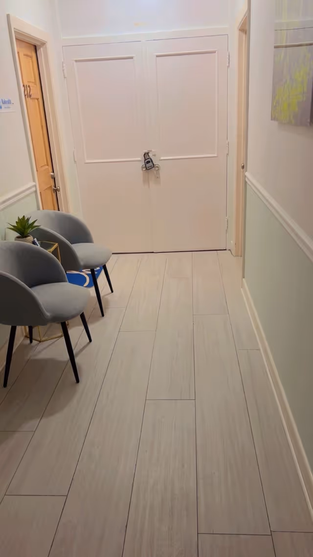 White interior hallway with gray tile floor, chairs, plant, and padlocked double doors.