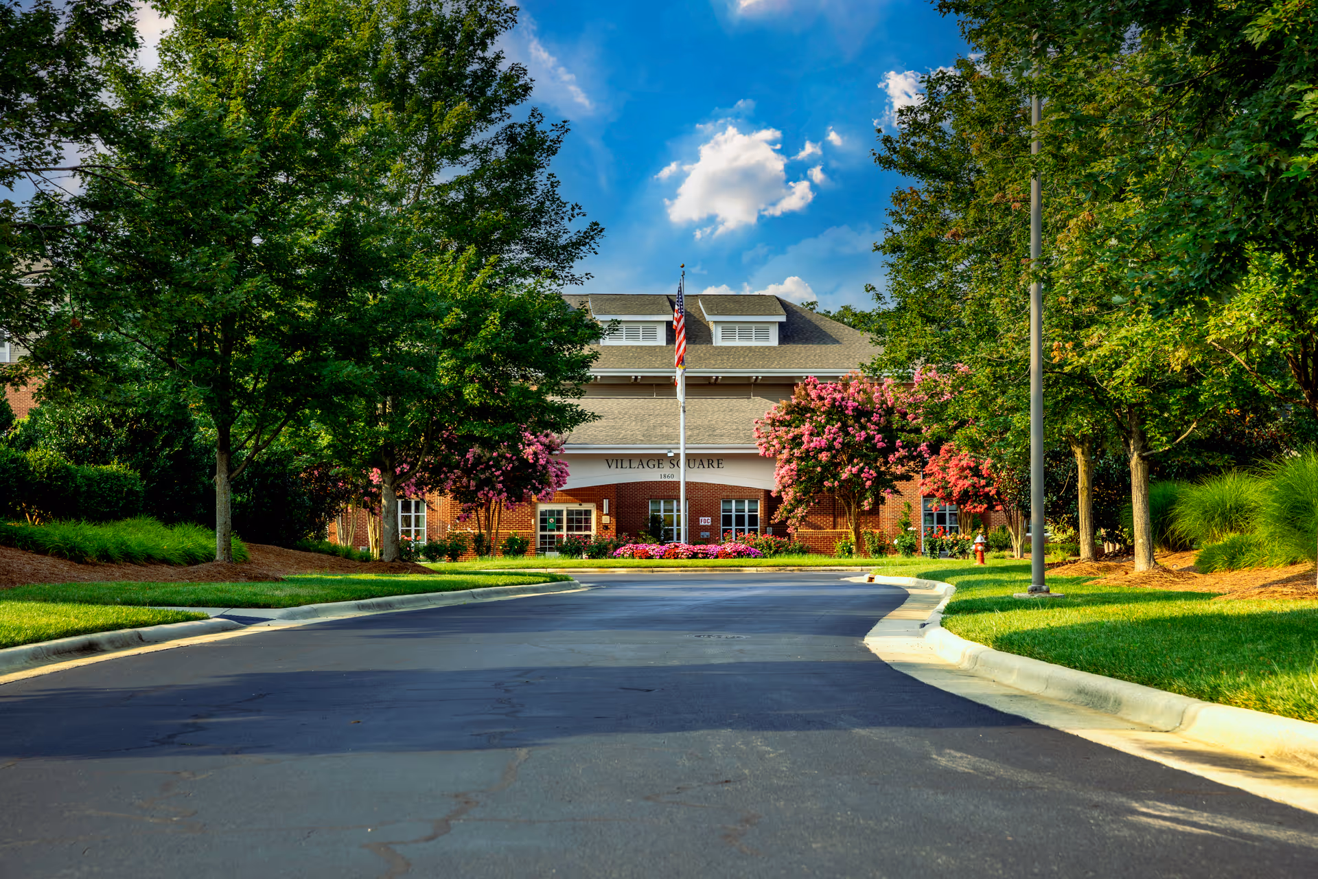 Front entrance of a senior living facility with a curved driveway, trees, and colorful landscaping.