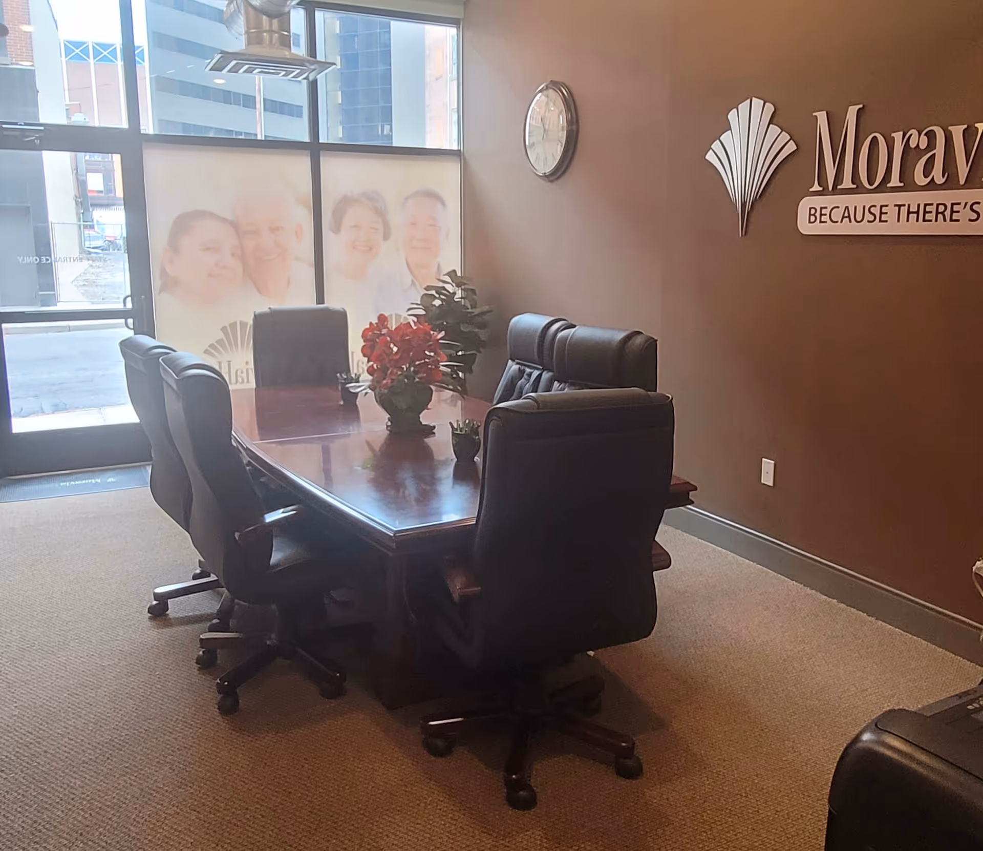 Conference room with a wooden table, black chairs, and Moravia Health signage on the wall.