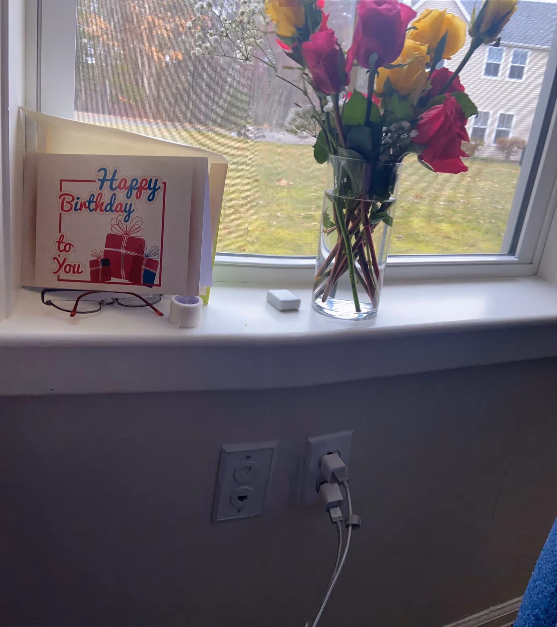 Indoor windowsill with a birthday card, colorful bouquet, and electrical outlets.