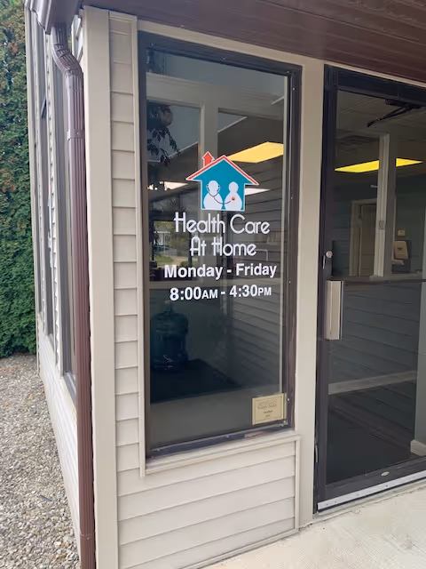 Exterior entrance of Health Care At Home, Inc. with logo and sign on glass door.