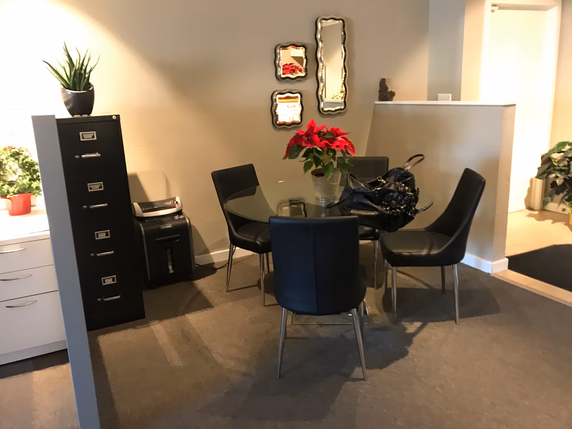 Small dining area with round glass table, black chairs, and poinsettia centerpiece.