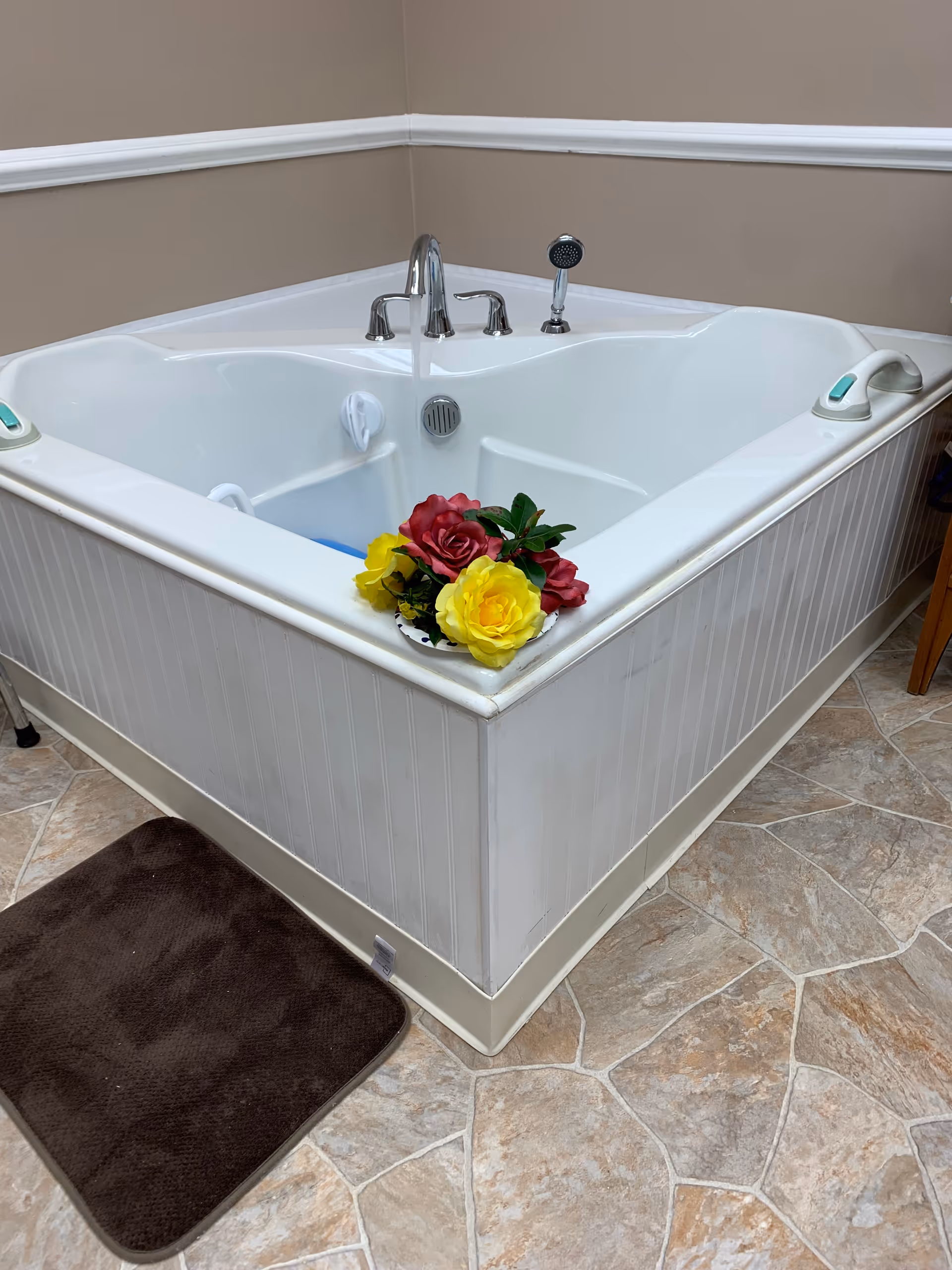 A white walk-in bathtub in a beige-tinted bathroom with a flower arrangement.