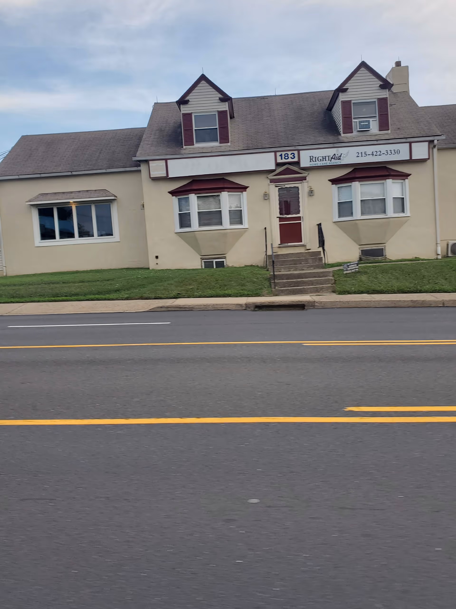 Exterior view of a beige, two-story Right Aid Home Care building with steps on a street.