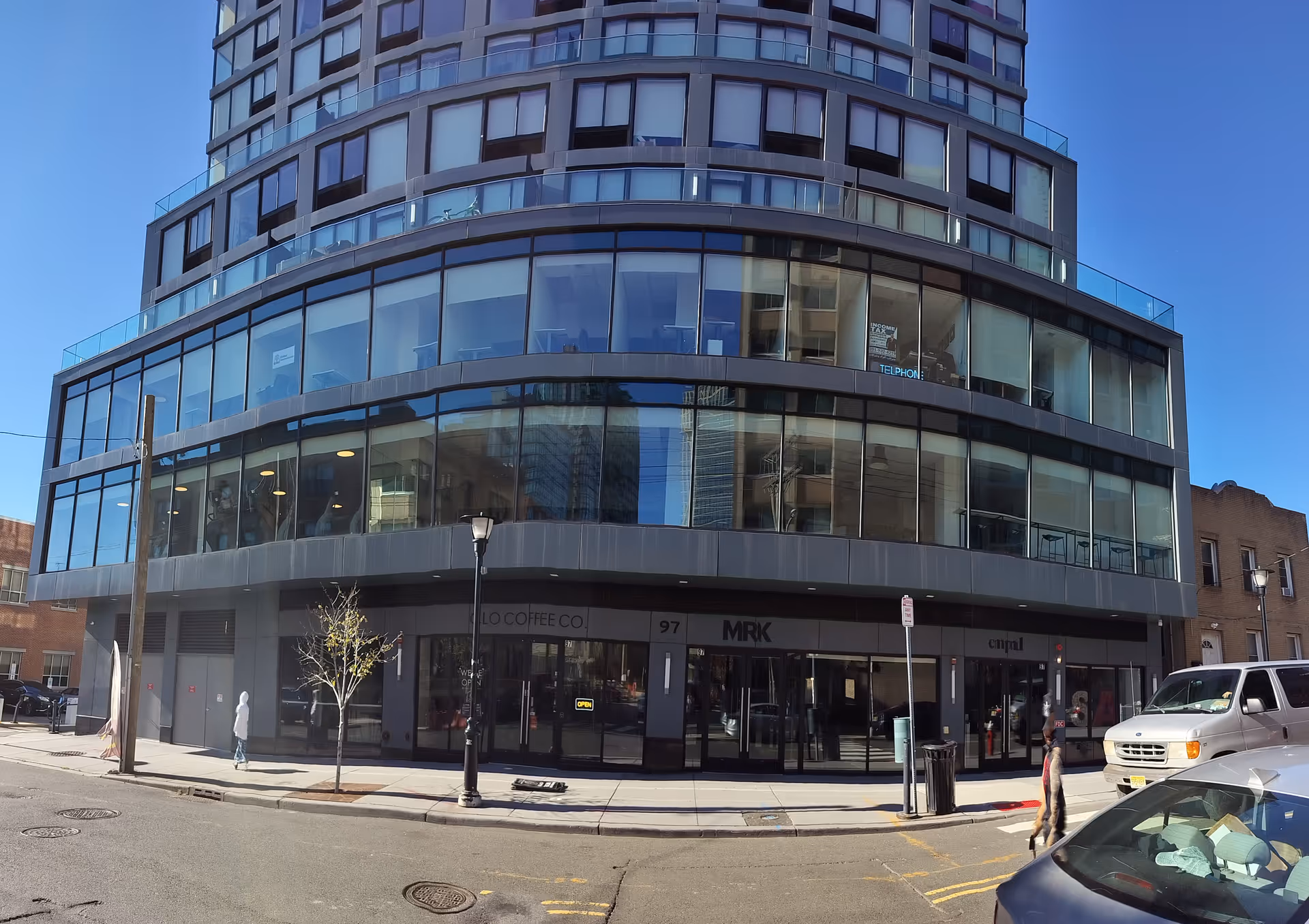 Tall glass-fronted building with curved, multi-story windows along a city street.