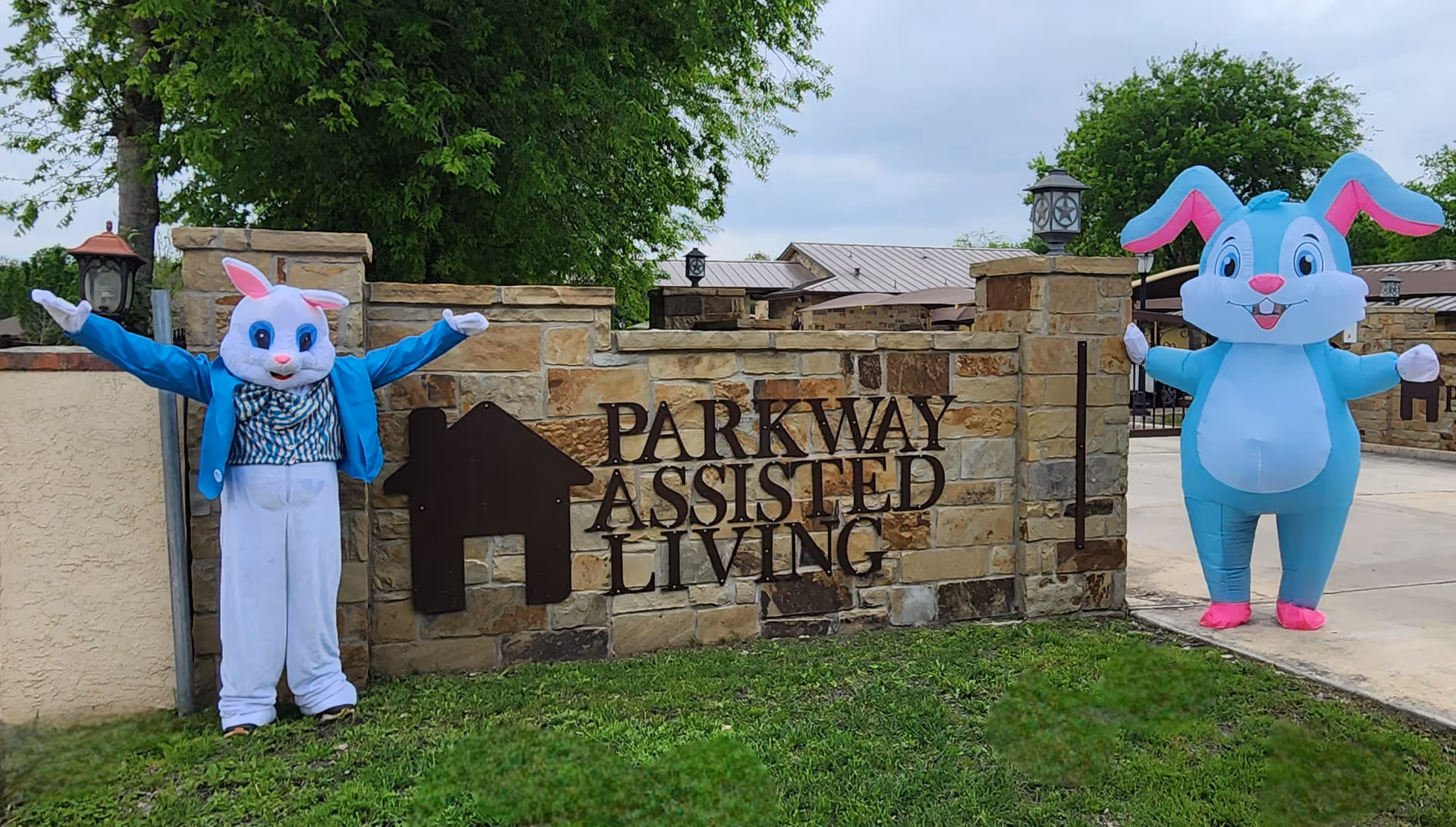 Two costumed rabbits stand beside a Parkway Assisted Living entrance sign outside.