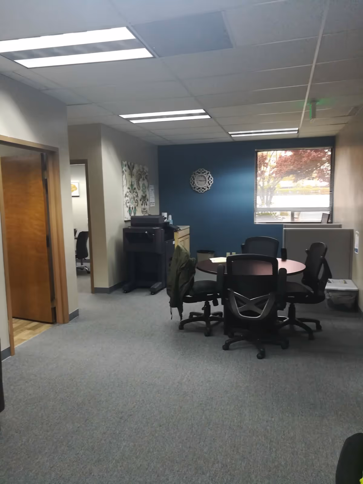 Office-like interior with round table, chairs, copier, and blue accent wall inside facility.