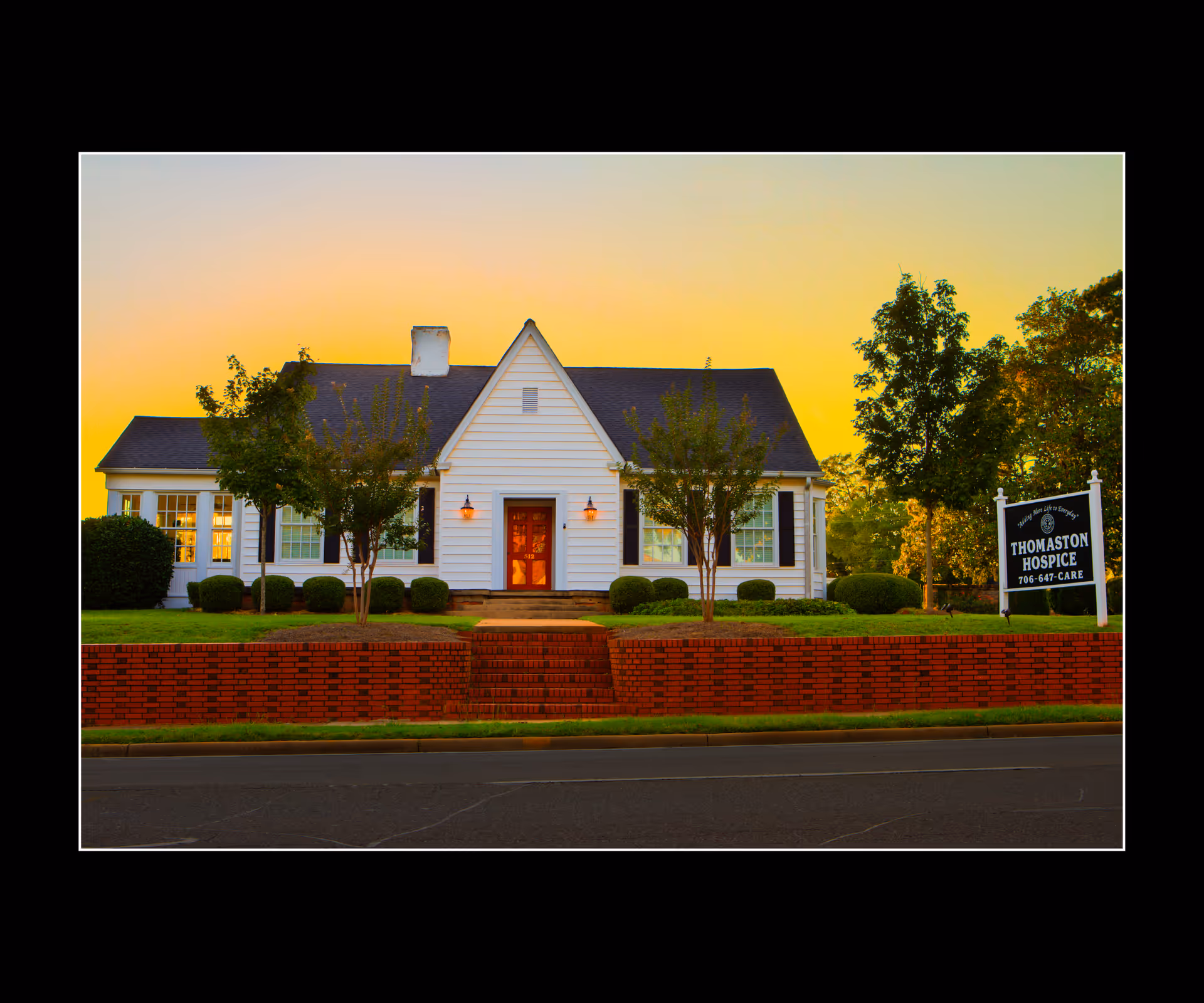White single-story building with a front entrance, lawn, trees, and a Thomaston Hospice sign.