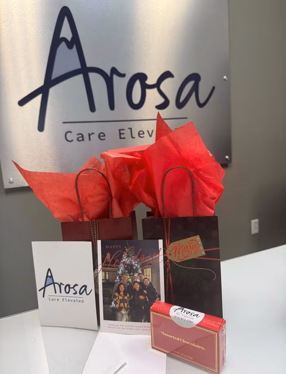 Arosa Care Elevated sign with gift bags, cards, and chocolates on a display counter.