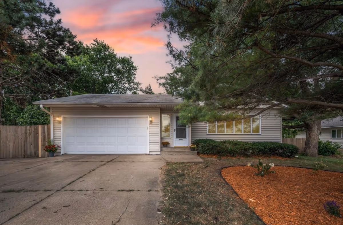 Single-story house with attached two-car garage, driveway, and landscaped front yard at sunset.