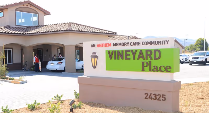 Entrance sign reading "Vineyard Place" in front of a single-story memory care community building with cars parked at the porte-cochère.
