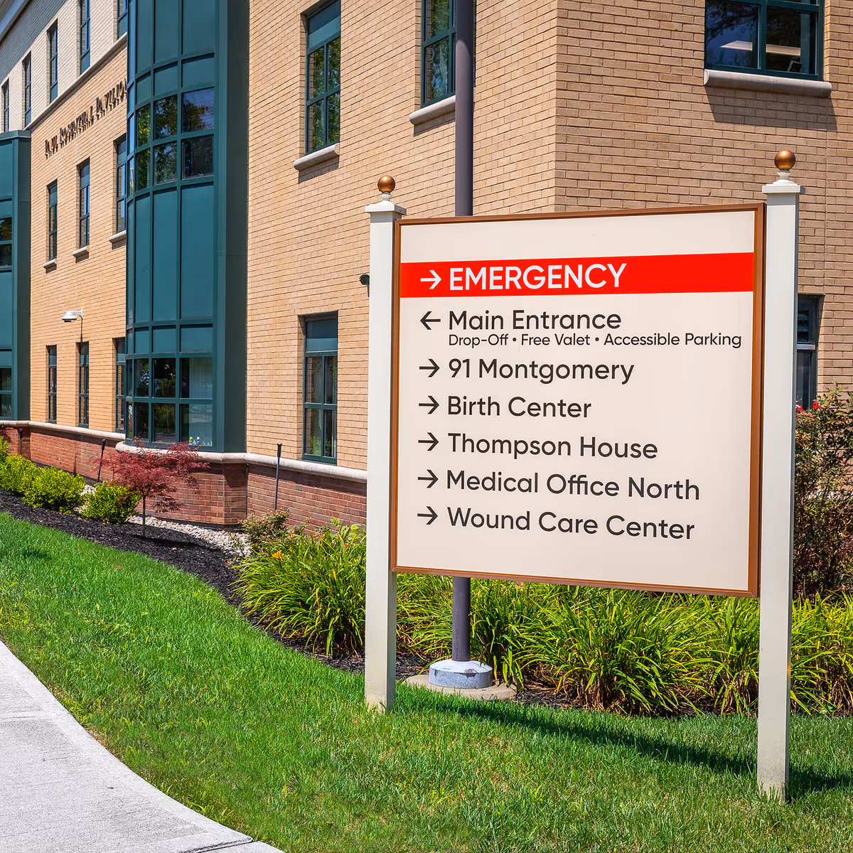 Exterior brick medical building with a large sign showing emergency and directions.