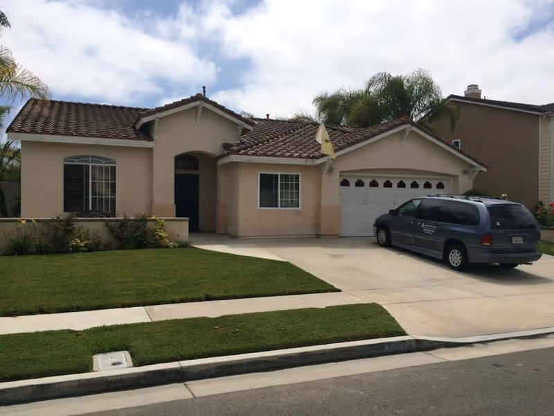 Front view of a beige suburban house with a parked van in the driveway.