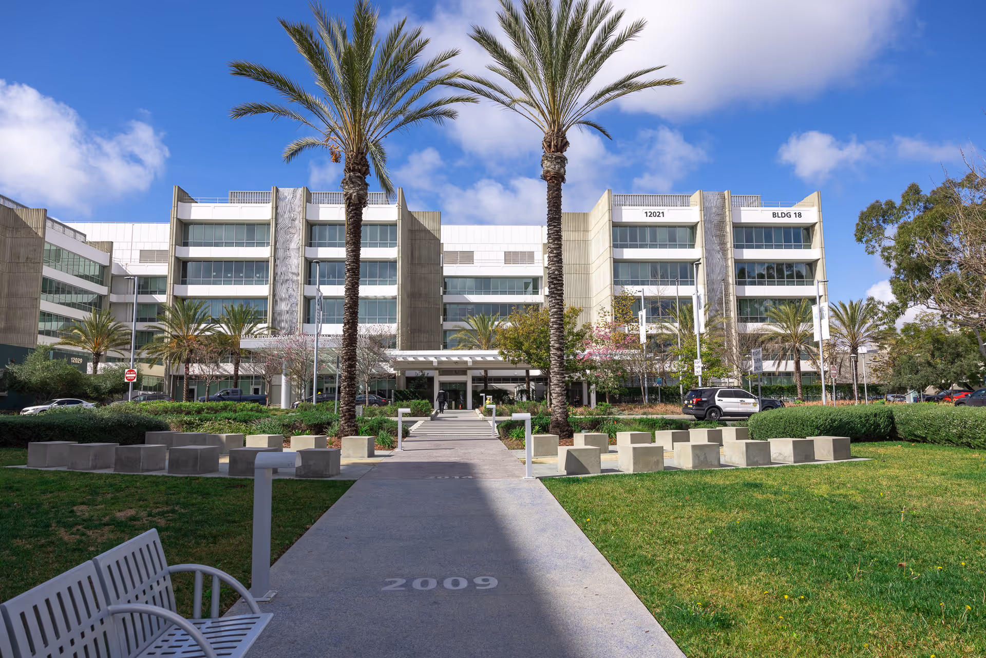 Front view of a multi-story senior living facility with a walkway and palm trees.