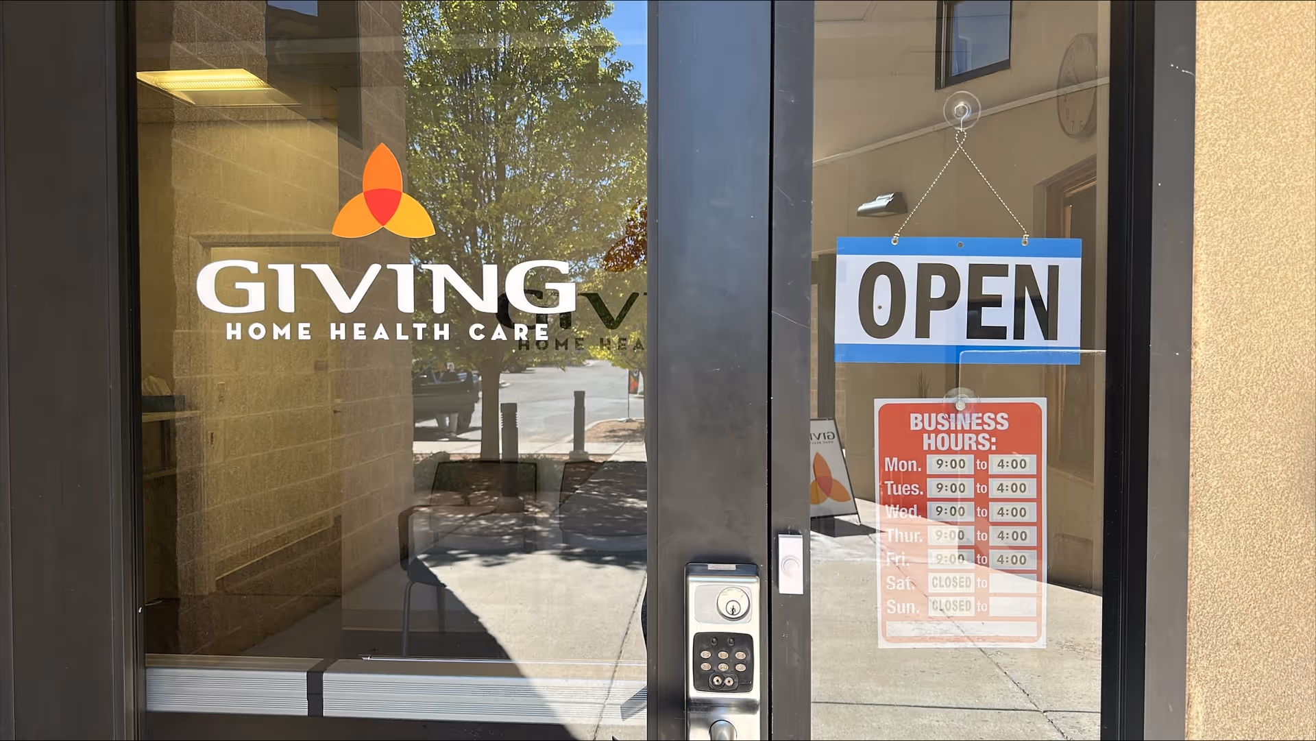 Glass storefront door for Giving Home Health Care with OPEN sign and hours.