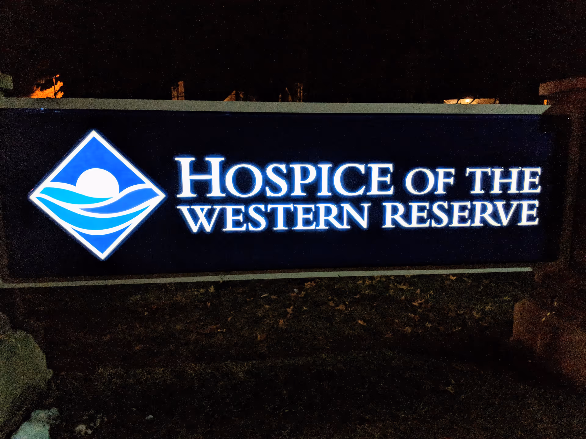 Night scene of an illuminated sign reading Hospice of the Western Reserve with a blue logo.