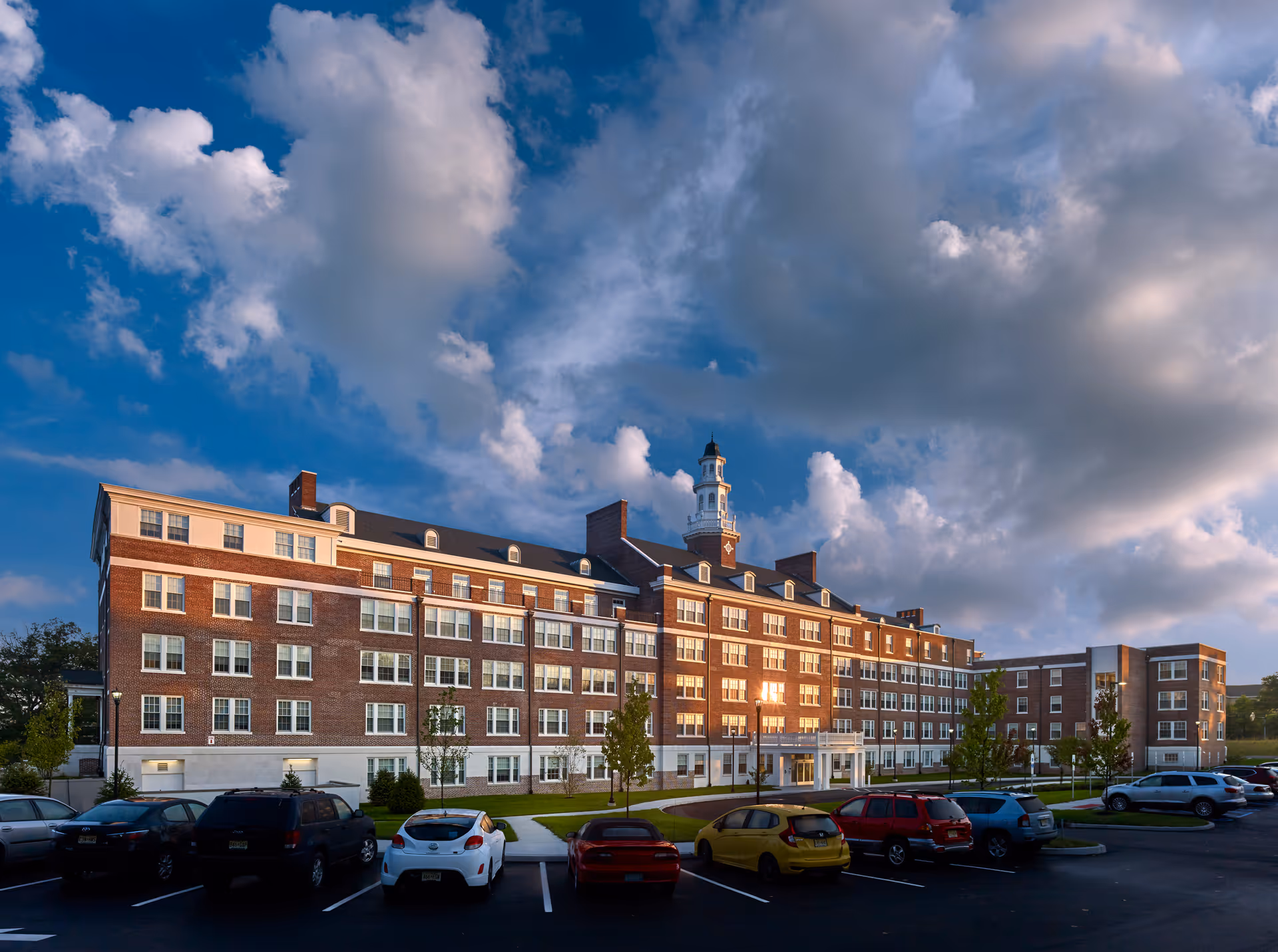 Exterior brick senior living building with a parking lot and a partly cloudy sky.