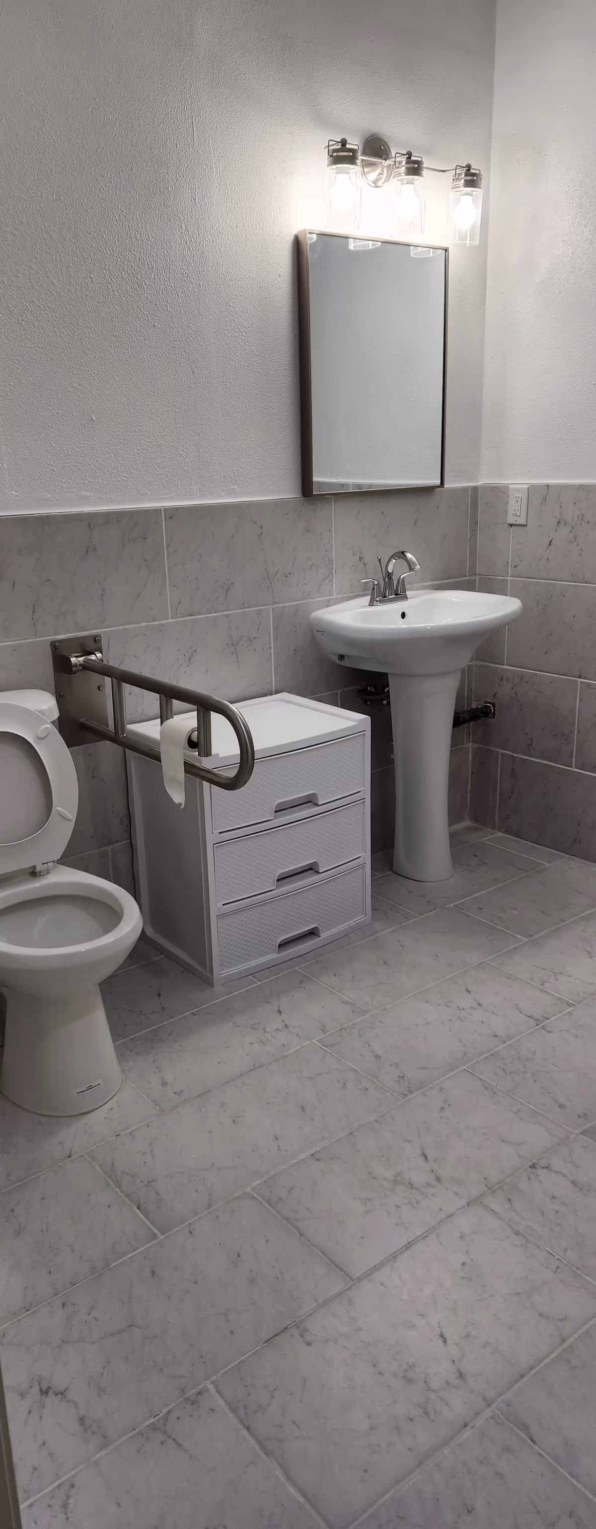 Public bathroom with toilet, pedestal sink, mirror, storage cabinet, and wall-mounted grab bar.