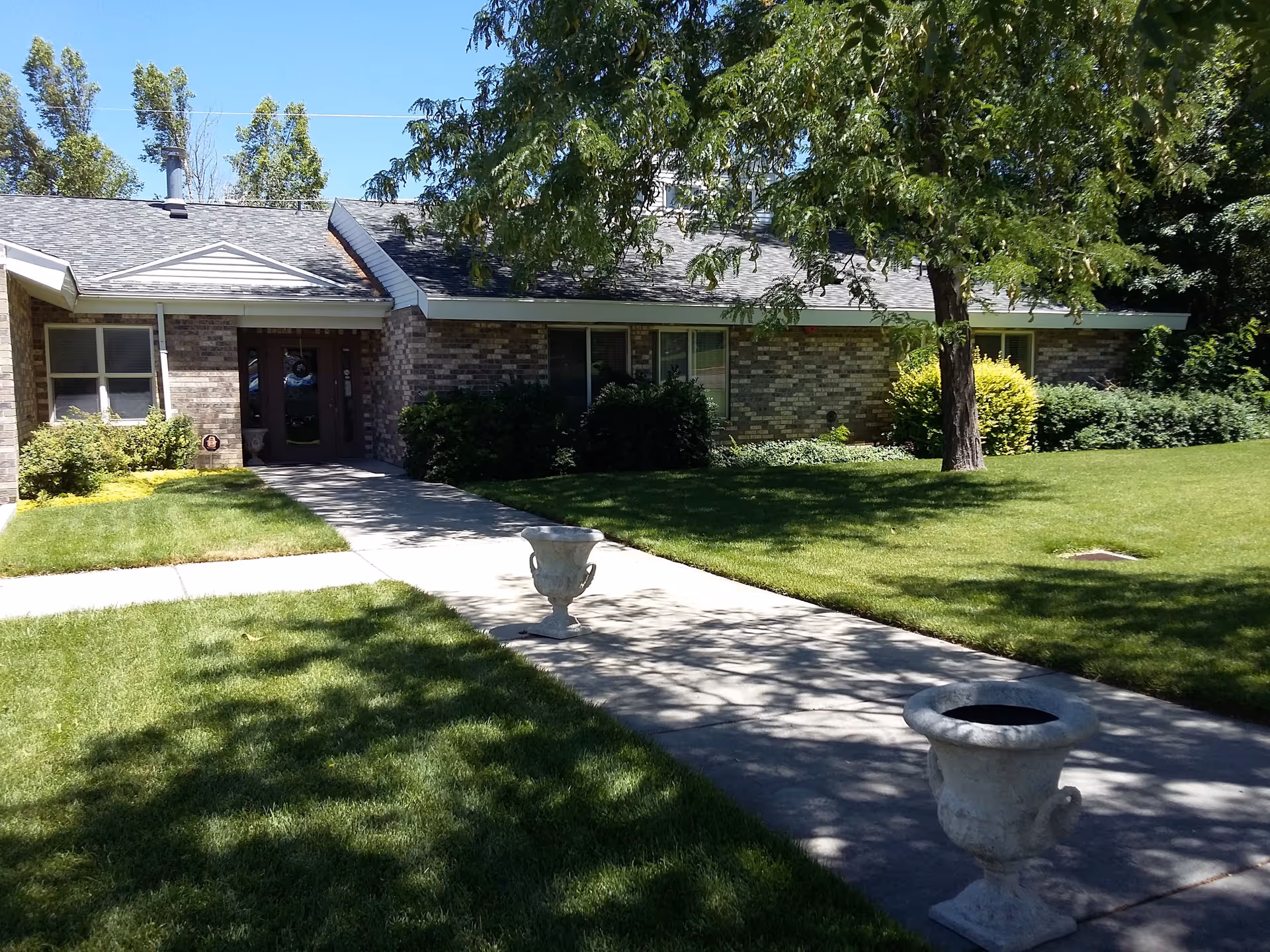 Brick senior living facility with a walkway to the entrance, manicured lawn, and trees.