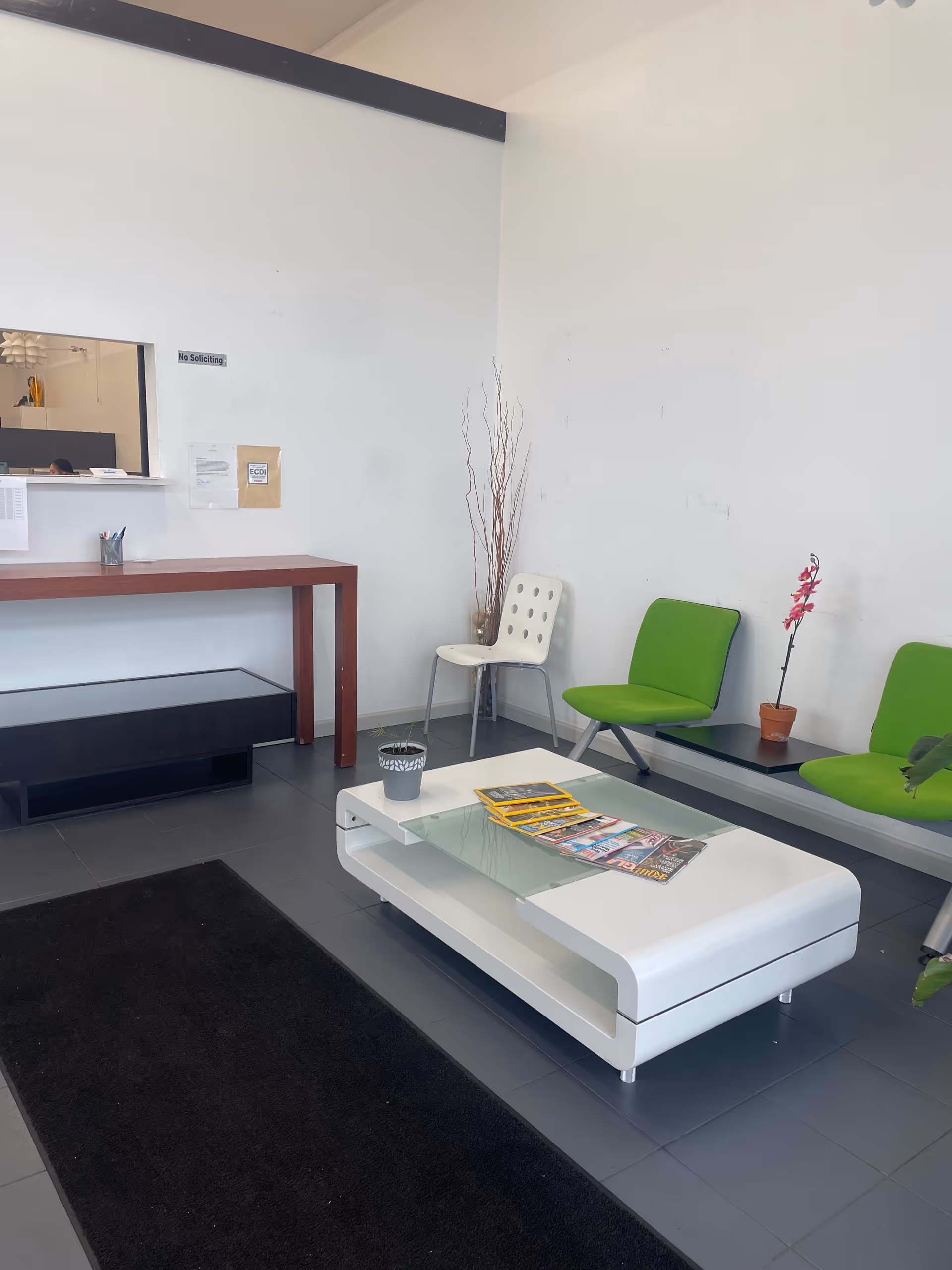 Modern waiting area with white coffee table, green chairs, and a reception window.