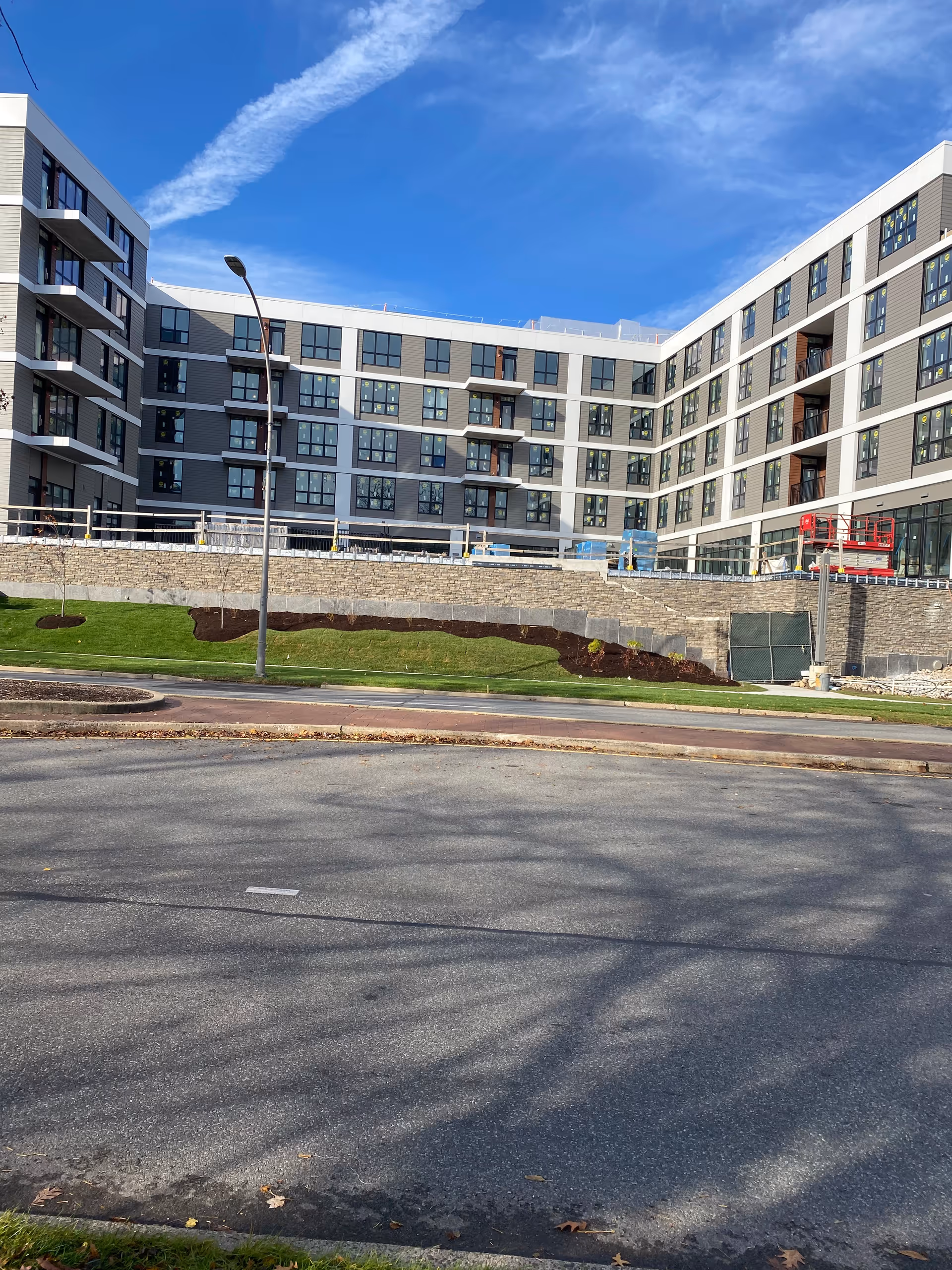 Modern multi-story senior living building with balconies along a street and landscaped slope.