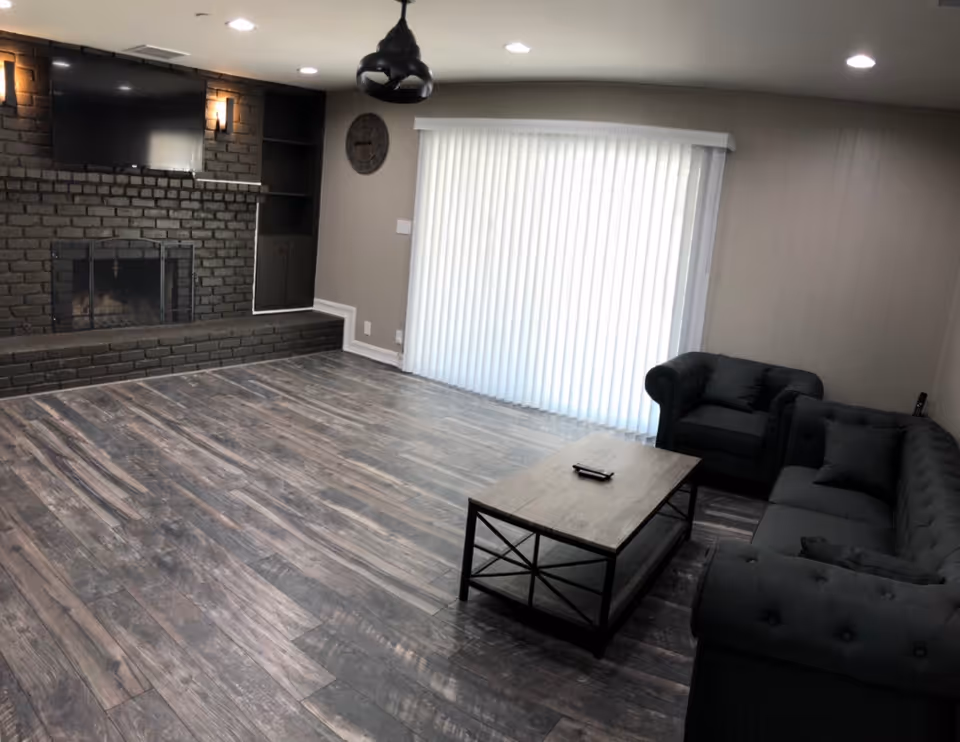 Interior lounge area with brick fireplace, dark couches, coffee table, and vertical blinds.