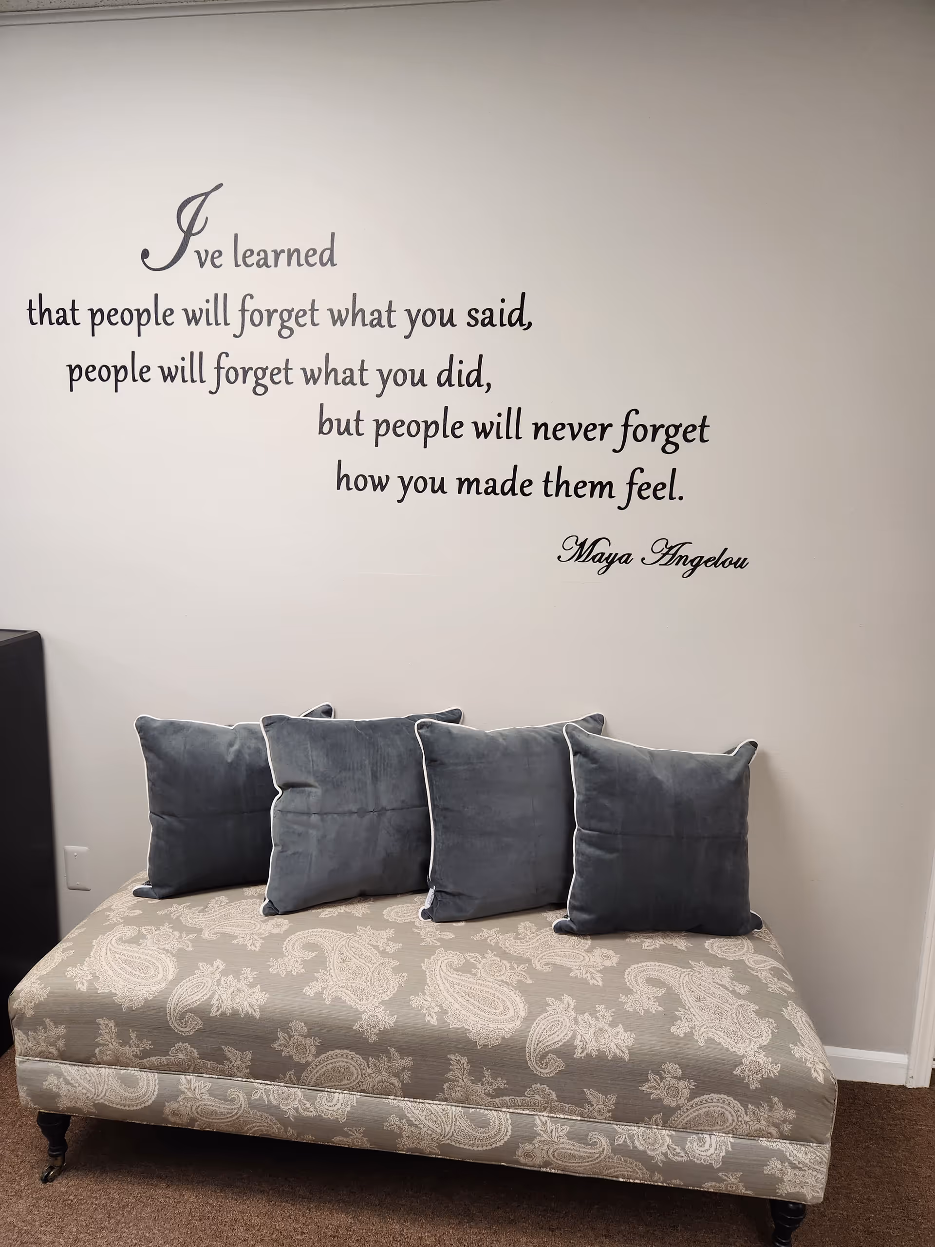 A patterned sofa with blue cushions sits beneath a wall quote in a cozy room.
