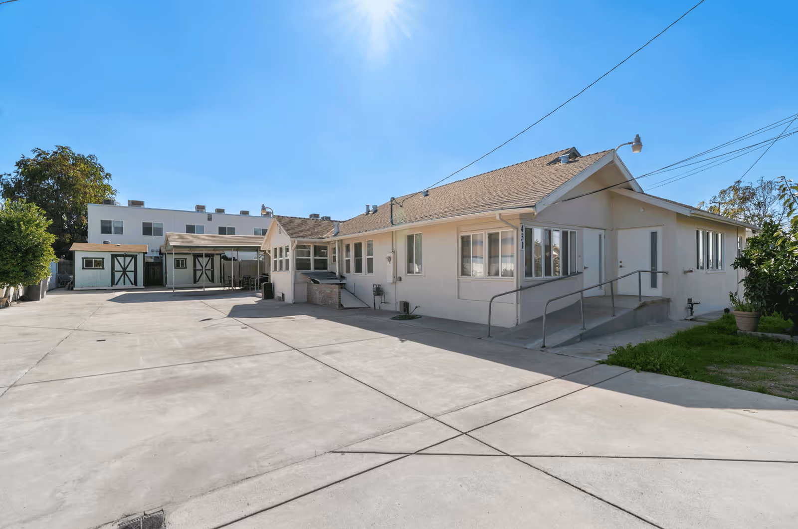 Exterior view of a single-story white senior care facility with a paved driveway and ramp.