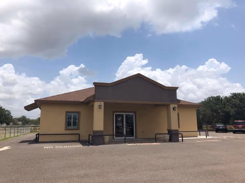 Front view of a single-story beige facility, Amigos Y Familia PHC, with covered entrance and parking.