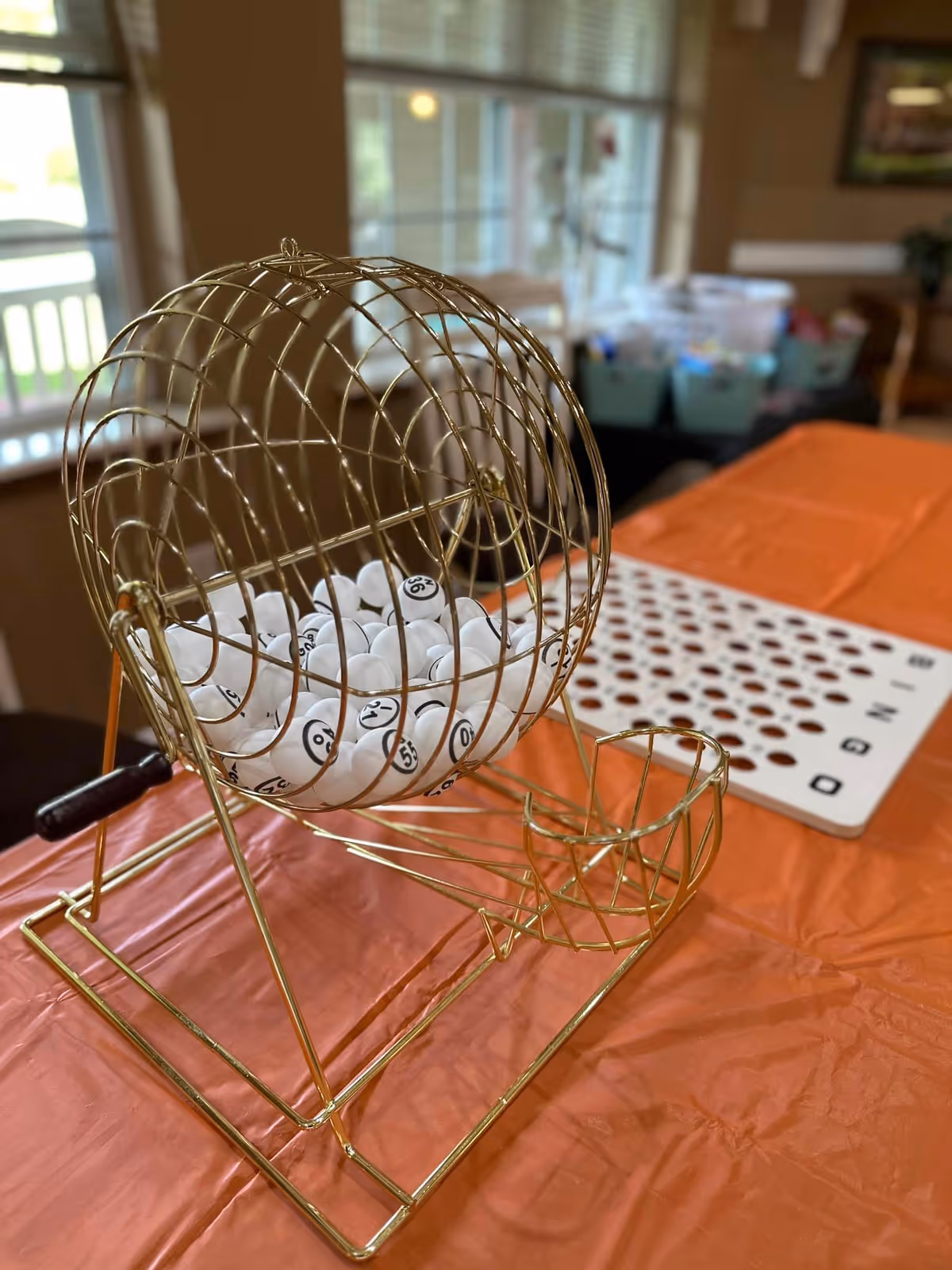 Gold bingo cage with numbered balls on an orange table in an indoor room