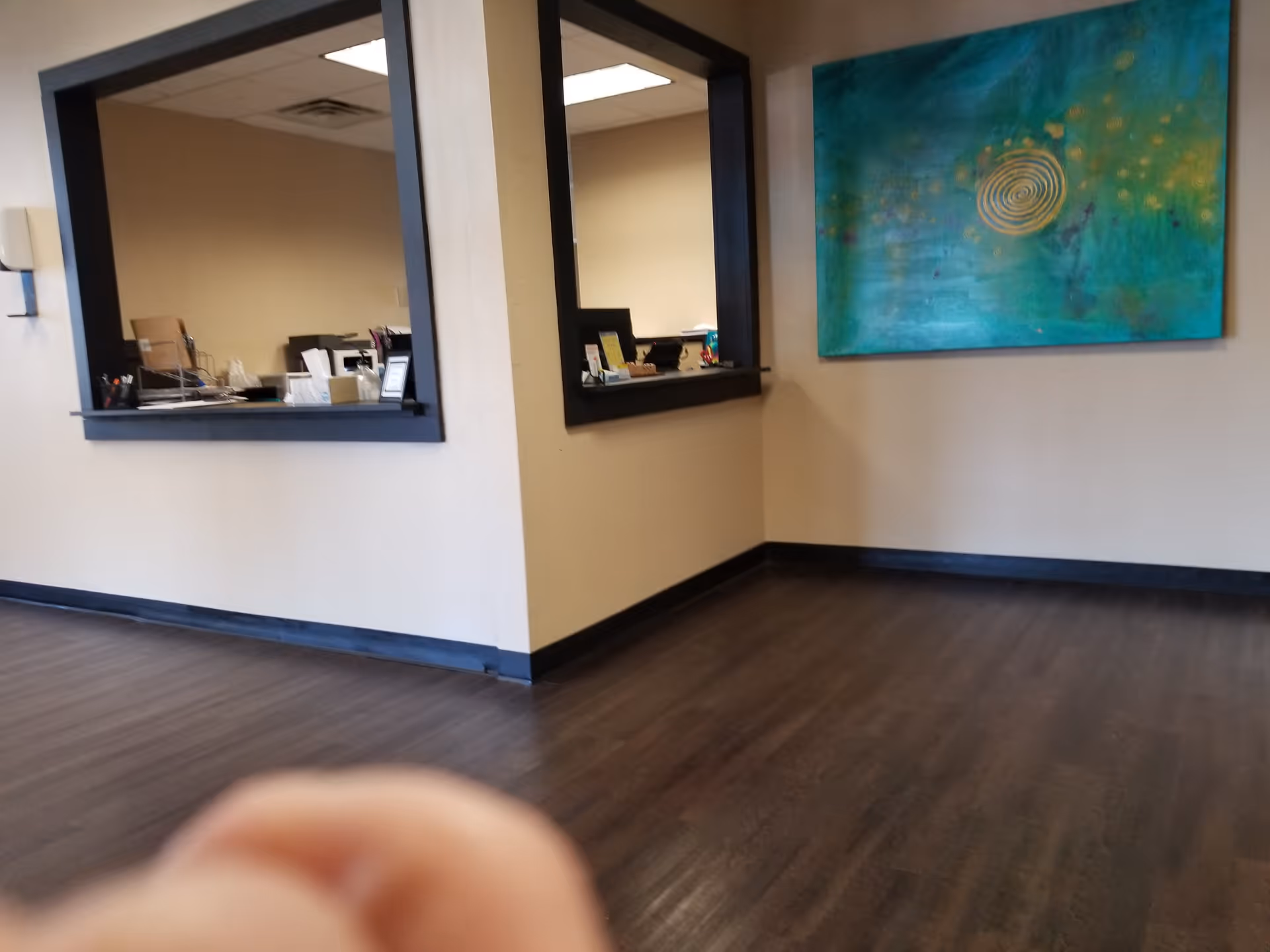 Interior lobby area with two service windows, abstract wall art, and dark wood flooring.
