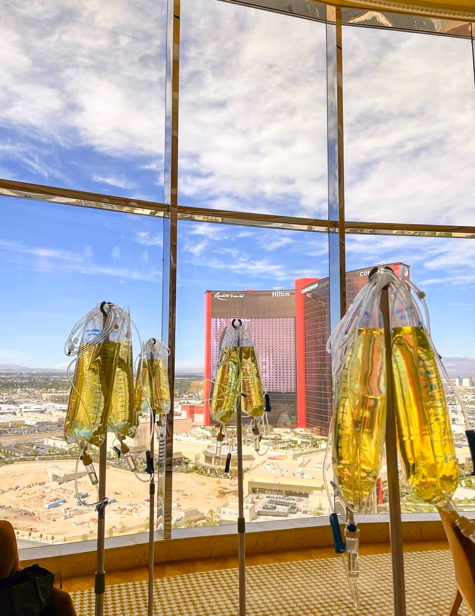 Multiple IV infusion bags on stands inside a bright room with a Las Vegas skyline view.