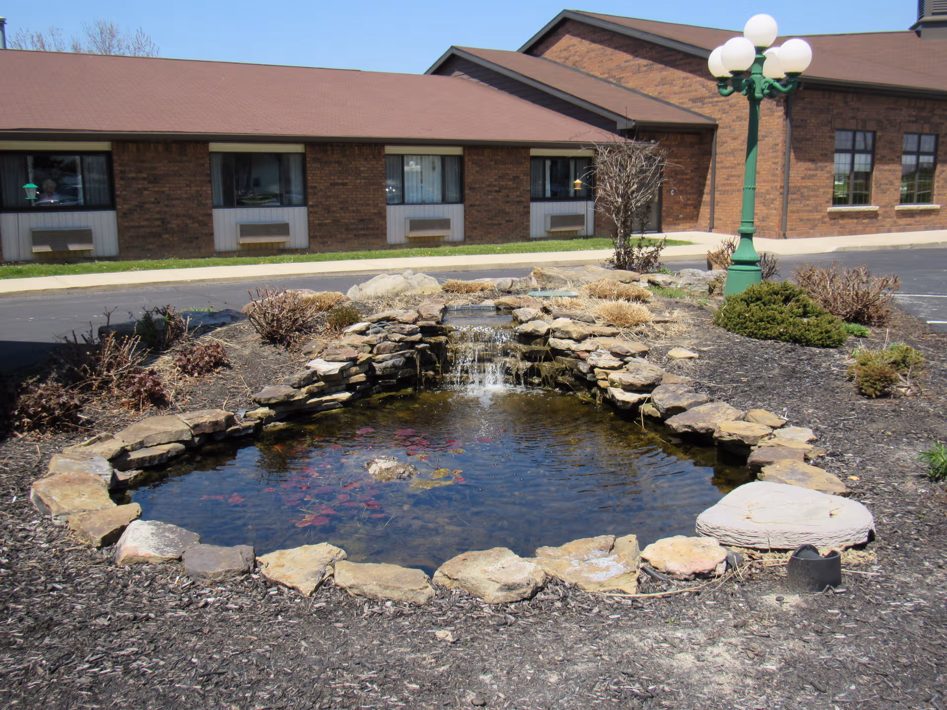 Brick senior living facility exterior with a landscaped pond and stone waterfall in front